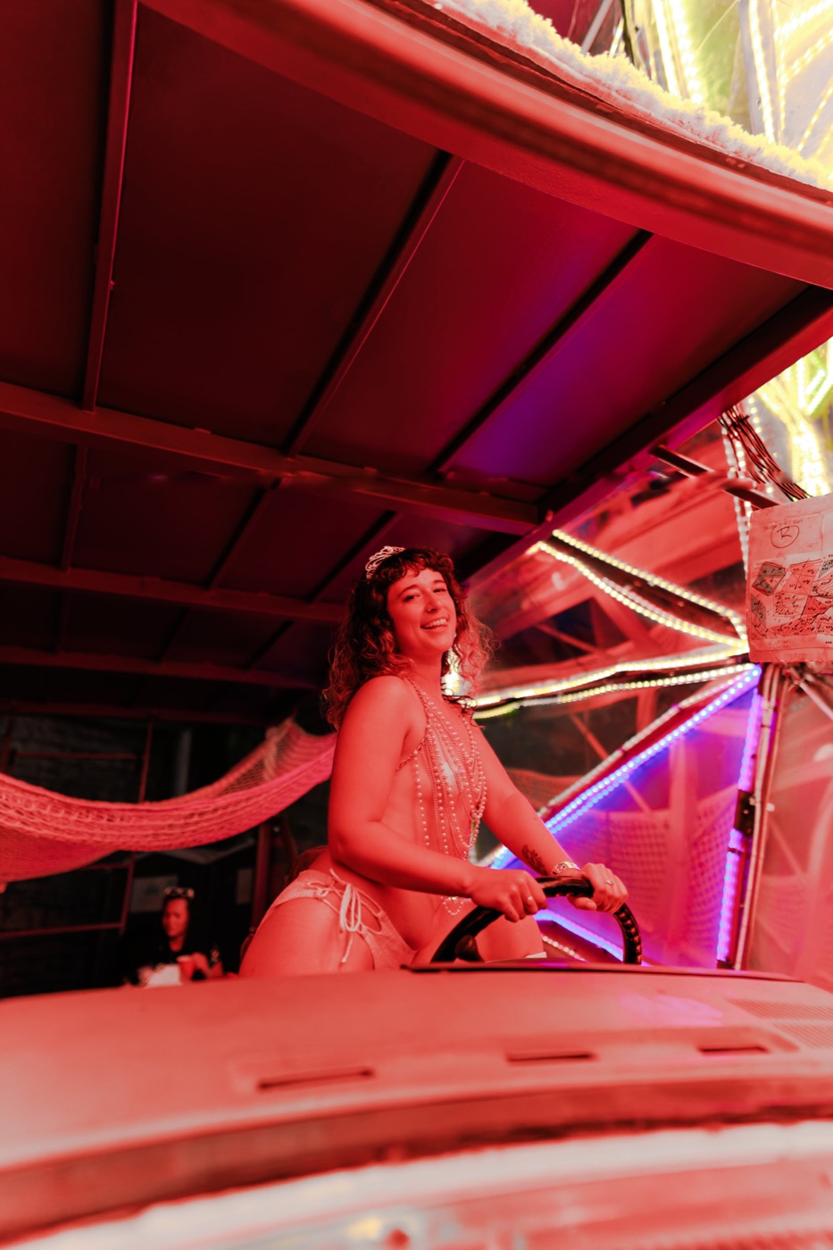 A dancer in pearls climbing onto the mirrored car under red and pink light