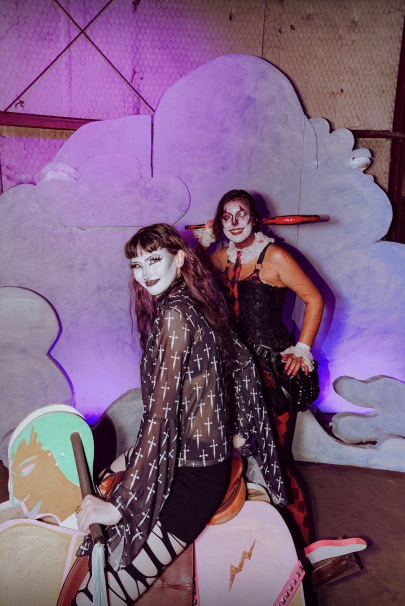 Two clowns posed on the rocking horse in front of painted clouds