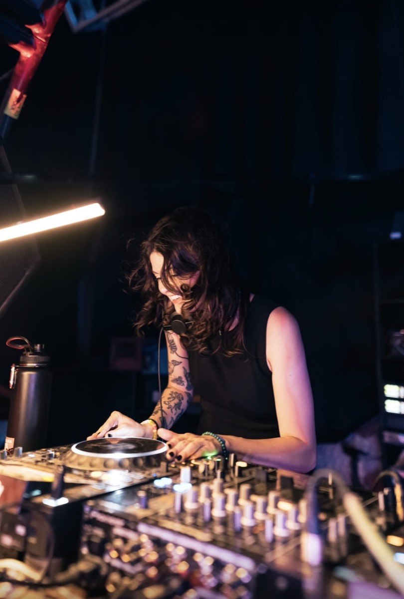 A DJ laughing over the mixer under the warehouse lights