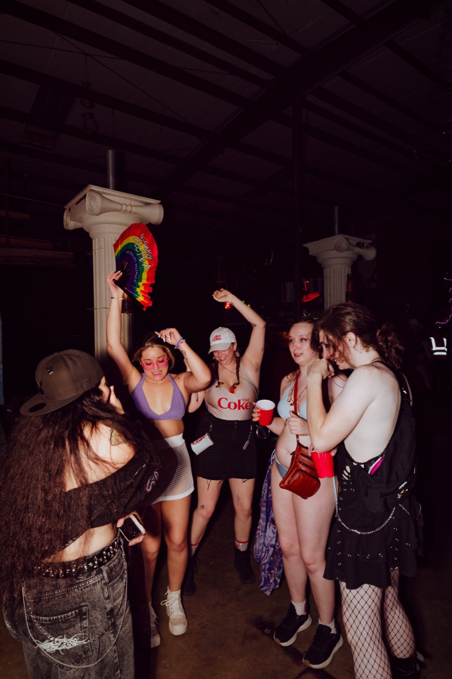 A crew dancing together between the columns, one waving a rainbow fan