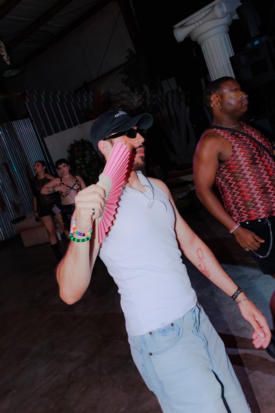A dancer in a white tank and cap strutting across the floor with a pink folding fan