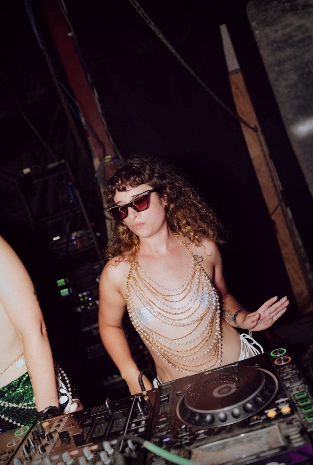 Hip Stir behind the decks at Babestock in a pearl-chain top and rhinestone sunglasses
